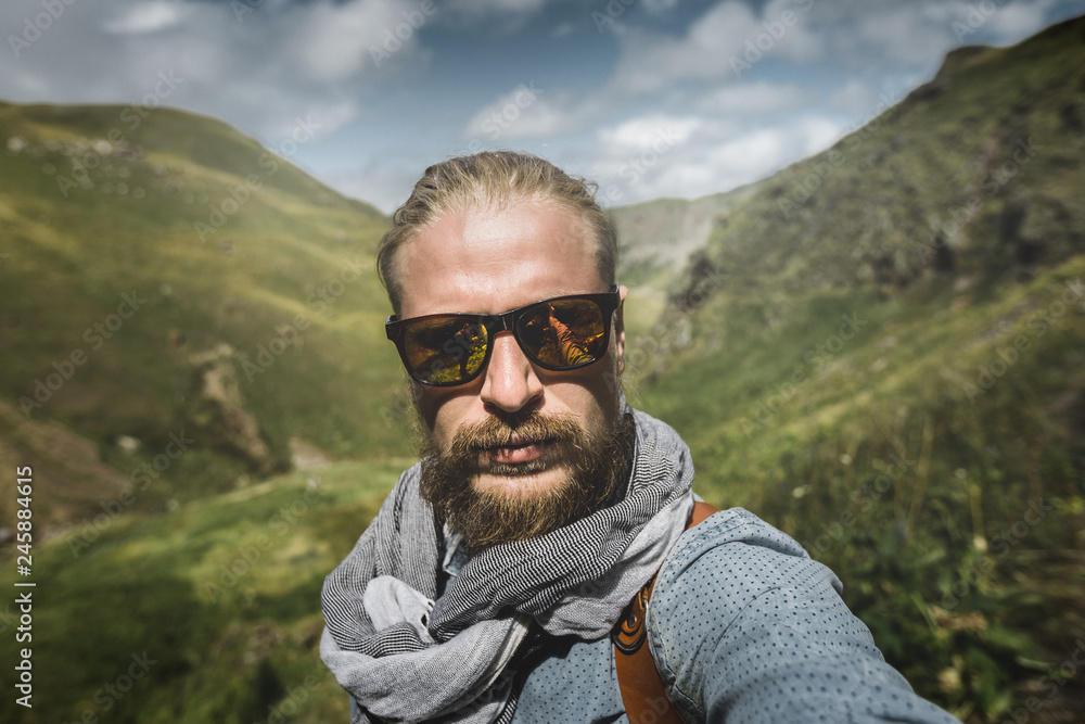 Global Travel Concept. Young Hiking Man In Sunglasses Take A Selfie On A Background Of A Mountain Landscape Global Travel Concept. Young Hiking Man In Sunglasses Take A Selfie On A Background Of A Mountain Landscape