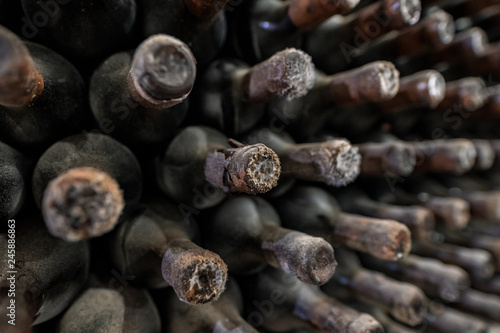 Detail of a dusty old wine bottle aging in a rack surrounded by other old wines