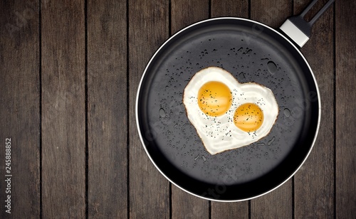 Fried egg with two yolks in the form of heart in a pan on wooden background