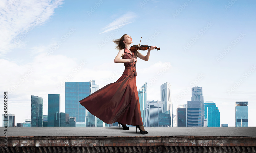 Valokuva Woman violinist in red dress playing melody against cloudy sky
