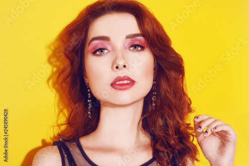 Fashion girl portrait on yellow background posing. Pretty brunette girl with long cerly hair and pink make up. Girl with long earrings. Portrait fashion model . Woman with pink make up. Beauty concept