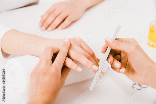 Partial view of manicurist holding fingers while doing nail form