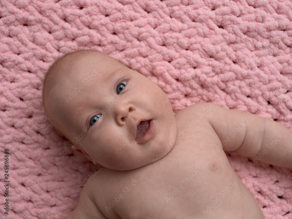 baby with a surprised face with open mouth. The baby lies on a pink micro-polyester rug. baby with a surprised face with open mouth. The baby lies on a pink micro-polyester rug.