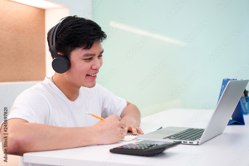 close up young asian student man wearing headset and looking at laptop display for learning mathematics online course from education website , writing lecture on notebook and solve lesson at library c close up young asian student man wearing headset and looking at laptop display for learning mathematics online course from education website , writing lecture on notebook and solve lesson at library c