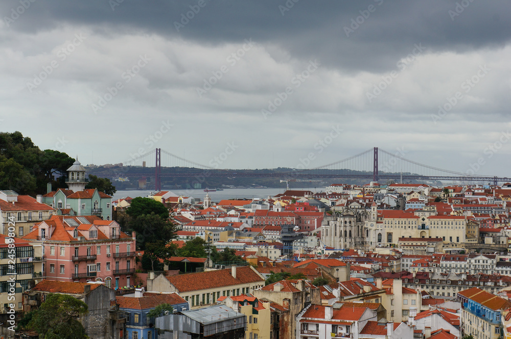 Roof top view over the city of Lisbon with colourful houses, red rooftops and the Vasco da Gama Bridge. Cityscape from Miradouro da Graça viewpoint, a well known gathering point for tourists.