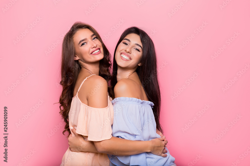 Excited girls embracing on pink studio background Excited girls embracing on pink studio background