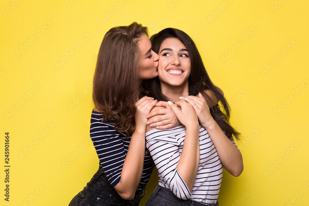 Happy girls embracing on yellow studio background Happy girls embracing on yellow studio background