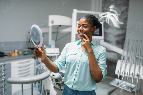 Patient looks on teeth in mirror, dental clinic