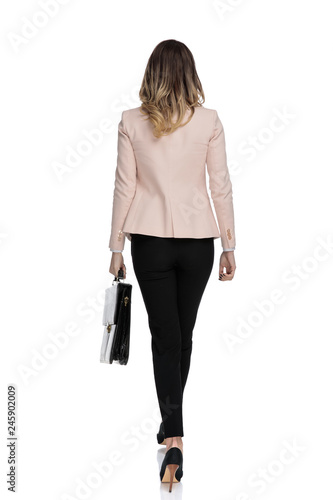 rear view of young businesswoman holding briefcase walking photo