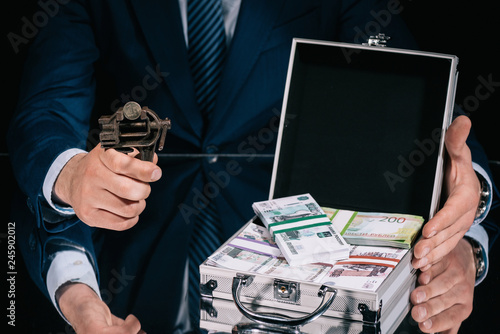 cropped shot of businessman holding iron vise tool with russian ruble coin and suitcase safe box with banknotes