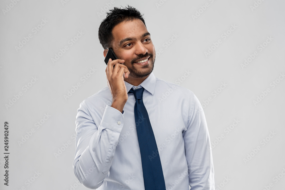 business, office worker and people concept - smiling indian businessman calling on smartphone over grey background business, office worker and people concept - smiling indian businessman calling on smartphone over grey background