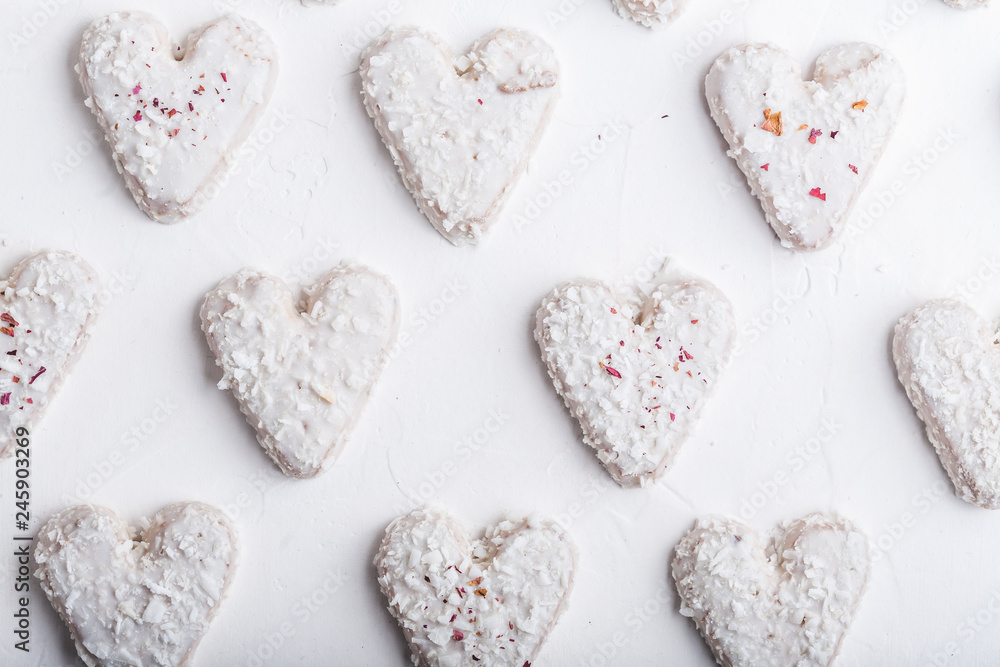 Fototapeta premium A pattern of Valentine's day white coconut heart shaped cookies on a white background with red sprinkles. Copy space. Monochrome