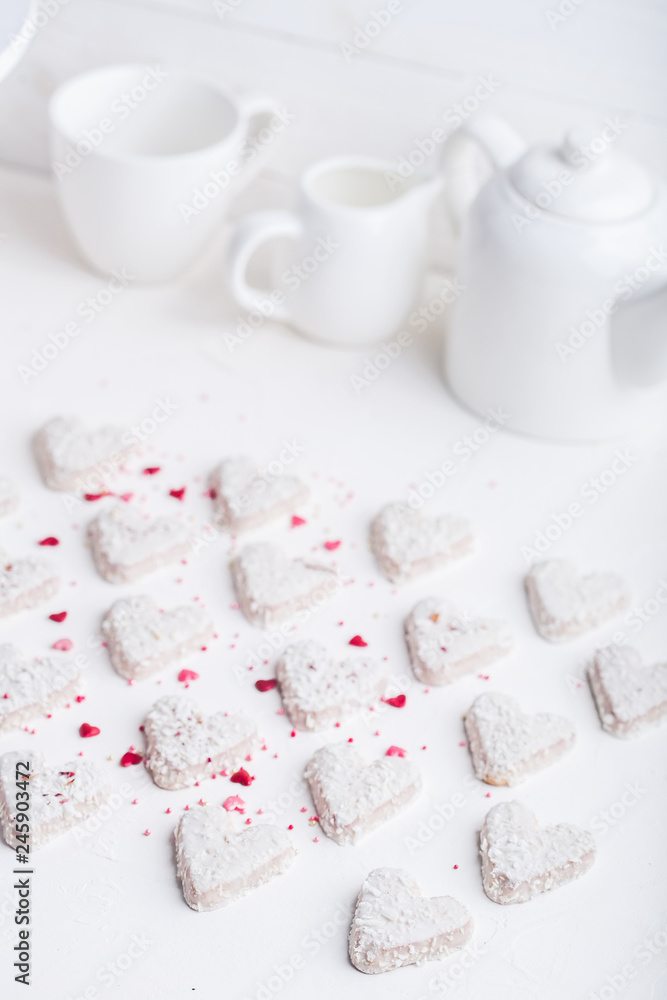 A pattern of Valentine's day white coconut heart shaped cookies on a white background with red sprinkles. Copy space. Monochrome A pattern of Valentine's day white coconut heart shaped cookies on a white background with red sprinkles. Copy space. Monochrome