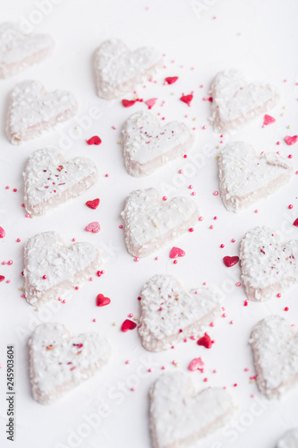  Valentine's day white coconut heart shaped cookies on a white plate with red sprinkles and white teapot. Copy space
