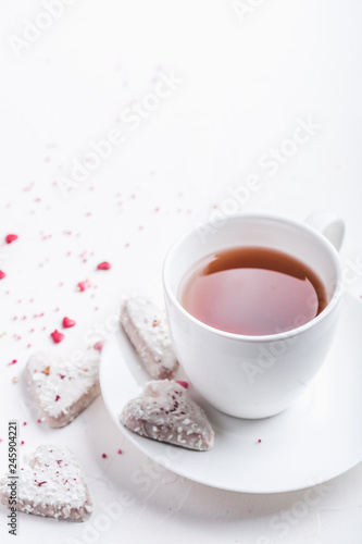  White tea cup with tea and Valentine's day white coconut heart shaped cookies with red and pink heart sprinkles. Copy space