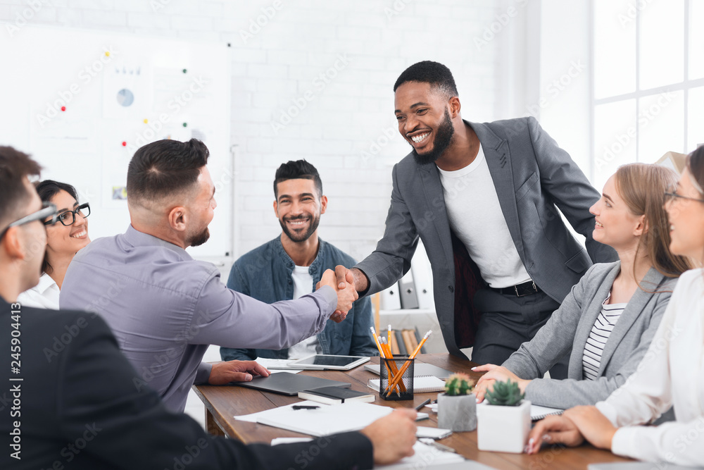 Two businessmen shaking hands, sitting at desk Two businessmen shaking hands, sitting at desk
