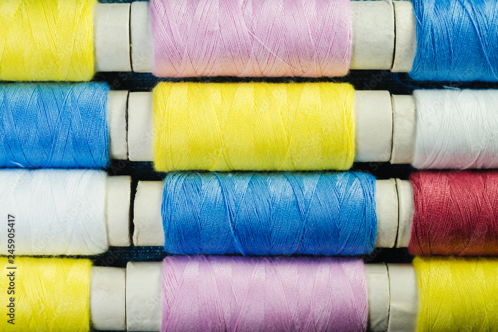 Spools of blue, yellow and pink sewing thread arranged in rows on denim Spools of blue, yellow and pink sewing thread arranged in rows on denim