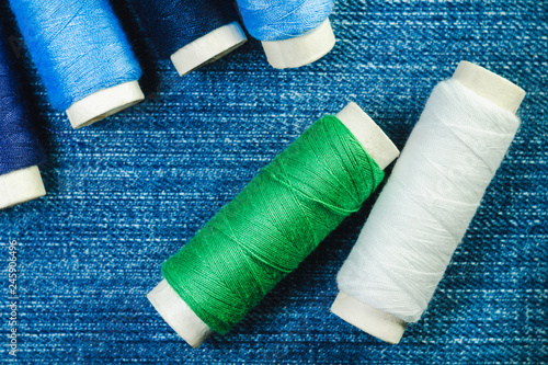 Spools of blue,white and green sewing thread on blue denim