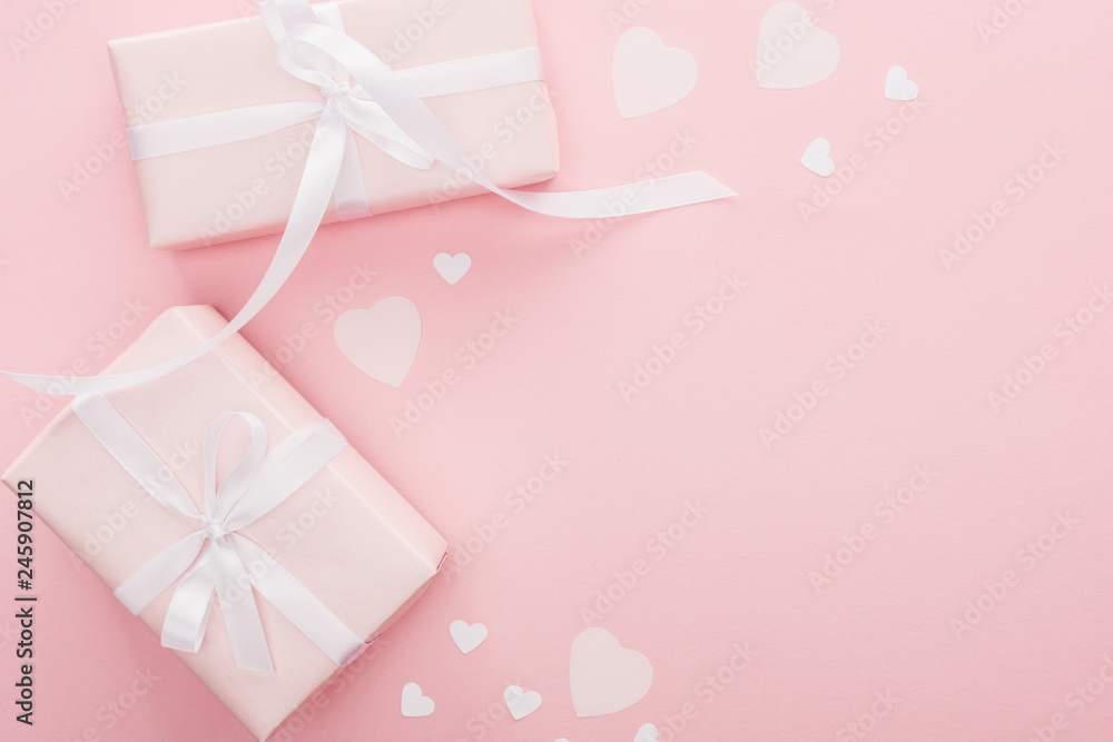 top view of gift boxes with ribbons and paper hearts isolated on pink with copy space