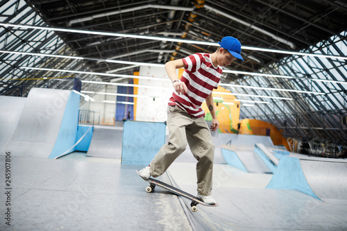 Active guy in casualwear standing on skateboard while descending along special parkour area or stadium