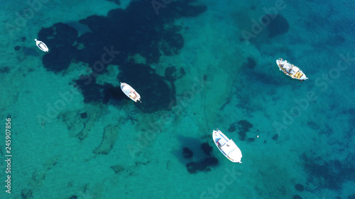 Aerial drone bird's eye view of small traditional fishing boat in port of Mykonos in sapphire clear waters, Cyclades, Greece