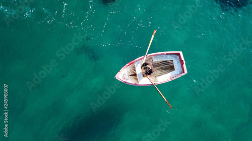 Aerial drone bird's eye view of small traditional fishing boat in port of Mykonos in sapphire clear waters, Cyclades, Greece