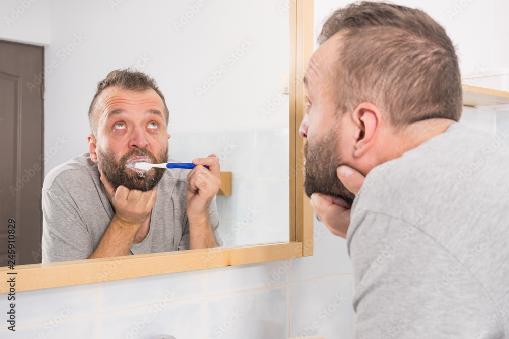Fototapeta premium Bored guy brushing his teeth in bathroom