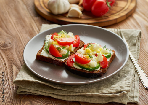 Smorrebrod - traditional Danish sandwiches. Black rye bread with boiled egg, cream cheese, cucumber, tomatoes on dark brown wooden background, side view