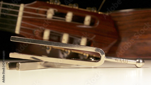 Tuning fork, two steel forks with classical guitars behind with strings, tuning keys, machine heads and headstock visible