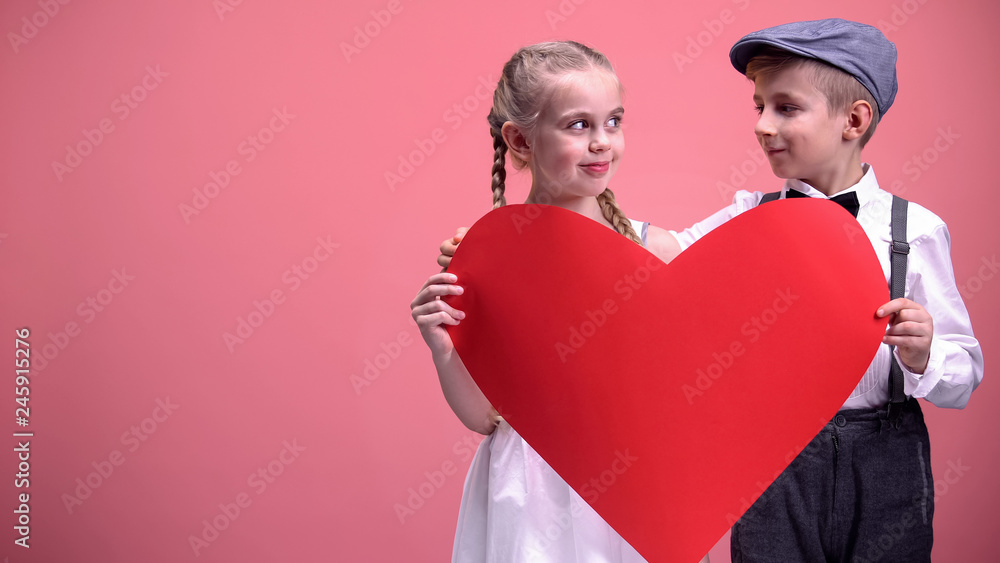 Little romantic kids holding red paper cutout and looking at each other, love Little romantic kids holding red paper cutout and looking at each other, love