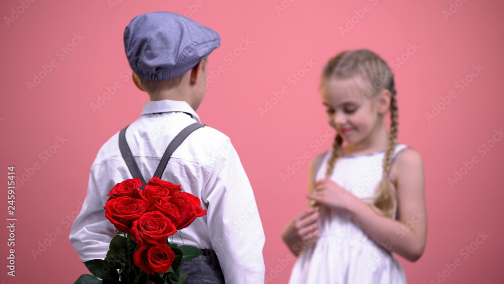 Young boy in formal clothes hiding roses behind back and presenting to girl Young boy in formal clothes hiding roses behind back and presenting to girl