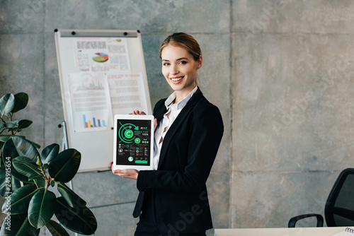 Pretty smiling businesswoman holding digital tablet with inphographics on screen photo