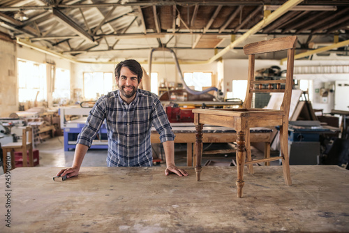 Smiling furniture maker sanding a chair on his workbench