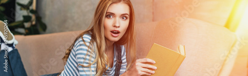 shocked young woman in room with sunshine holding book in hands