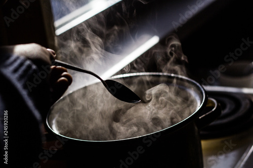 the man stirs the soup in the pan from which steam comes