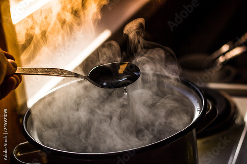 the man stirs the soup in the pan from which steam comes