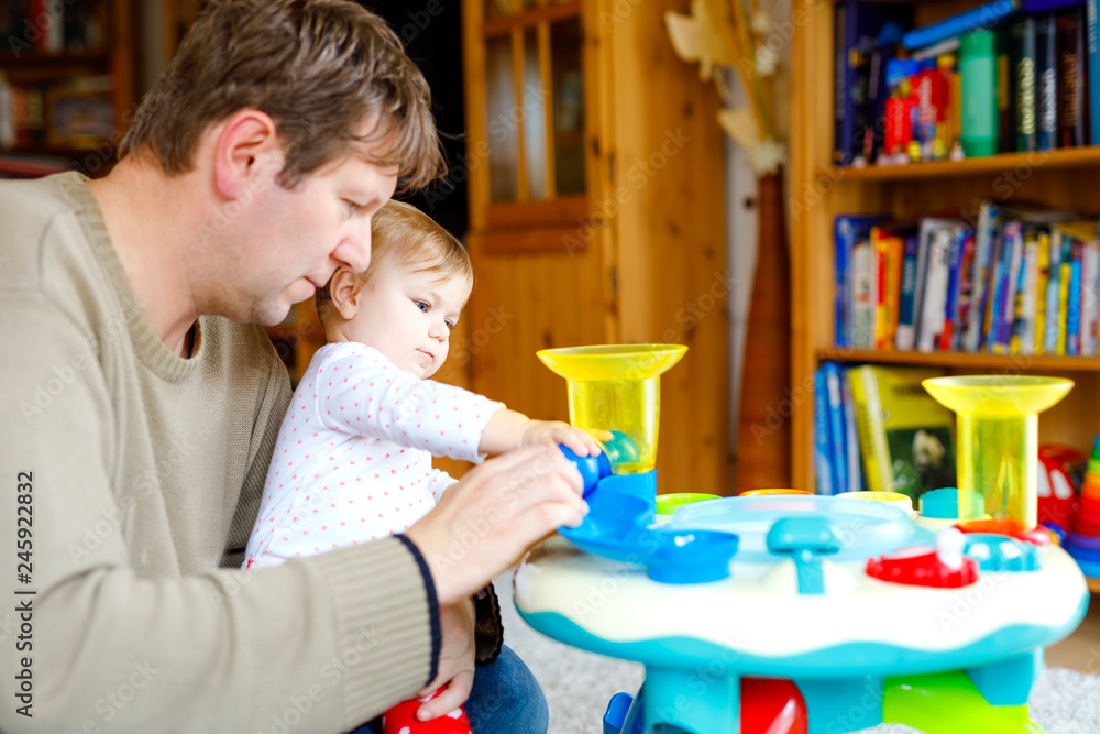 Obraz premium Happy proud young father having fun with baby daughter, family portrait together. Dad playing with baby girl with educational sorter toy with different colorful balls. Man with little child at home.