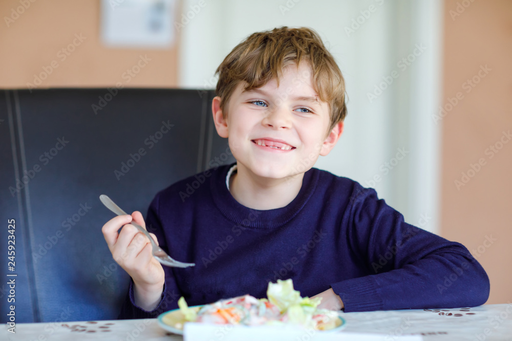 Happy kid boy eating fresh salad with tomato, cucumber and different vegetables as meal or snack. Healthy child enjoying tasty and fresh food at home or at school canteen. Happy kid boy eating fresh salad with tomato, cucumber and different vegetables as meal or snack. Healthy child enjoying tasty and fresh food at home or at school canteen.