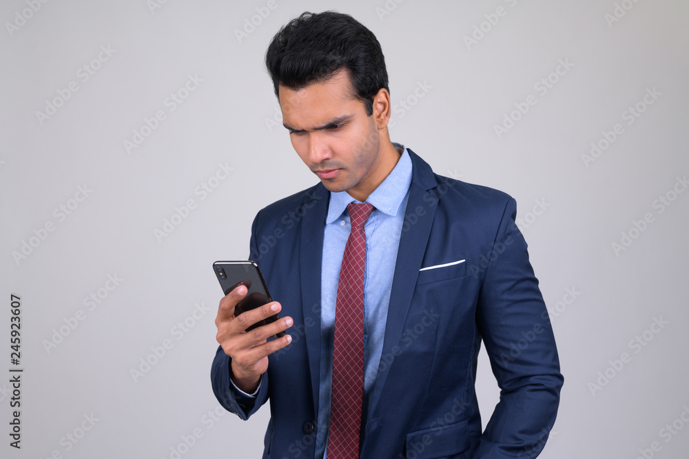 Portrait of young handsome Indian businessman using phone Portrait of young handsome Indian businessman using phone