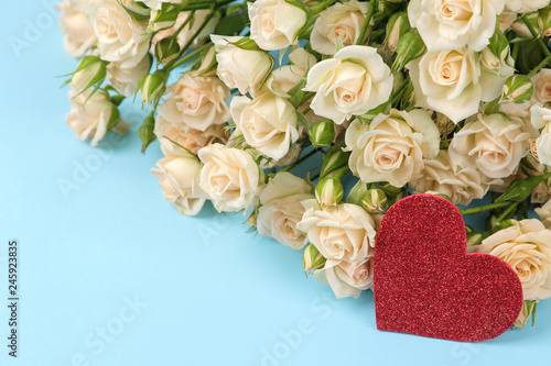 Beautiful mini roses with a red heart on a bright blue background. holidays. Valentine s Day. close-up