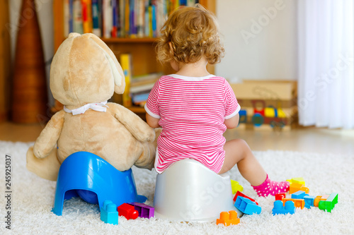 Closeup of cute little 12 months old toddler baby girl child sitting on potty. Kid playing with big plush soft toy. Toilet training concept. Baby learning, development steps