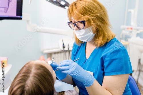 Woman dentist with glasses treats teeth of a young girl in the clinic close-up