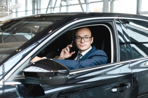Businessman sitting inside the cabin of a black car talking on the phone