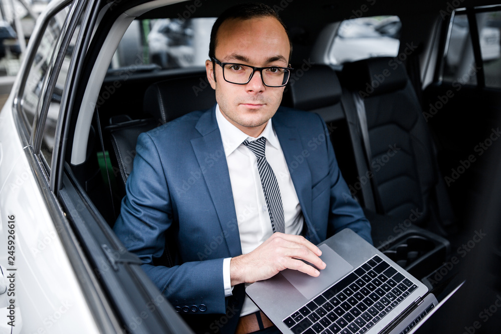 Businessman in a suit sitting in the back seat of a car working on a laptop typing on the keyboard