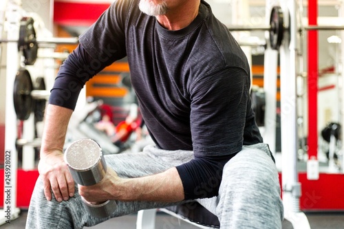 Gray-haired adult male athlete sitting on a bench with his hand raises a weight training muscles close-up photo