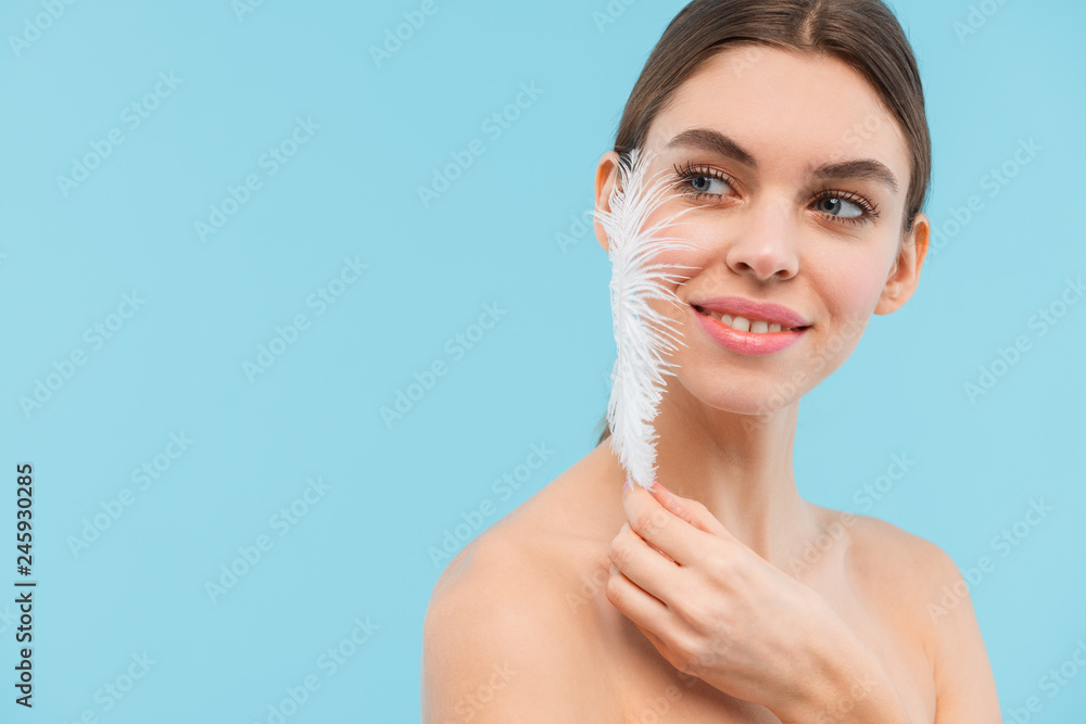 Beautiful young woman posing isolated over blue background holding feather. Beautiful young woman posing isolated over blue background holding feather.