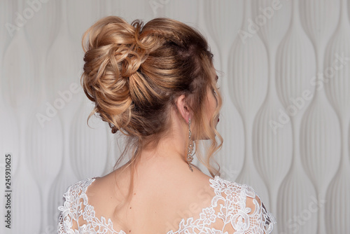 Wedding female hairstyle on the head of the girl blonde back view close-up on a light background.