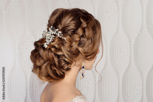 Wedding female hairstyle low beam on the head of a brown-haired girl back view on a light background.