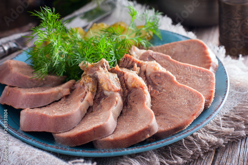 Chopped boiled beef tongue on a plate with fresh herbs and pickled cucumbers, horizontal