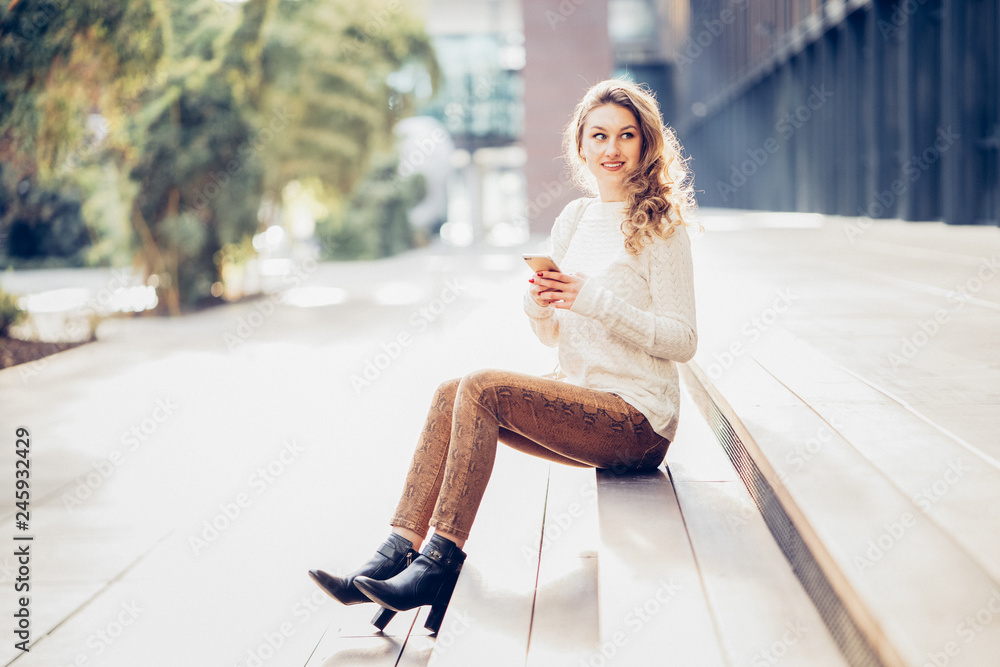 Schöne junge Frau sitzt in casual Kleidung draußen auf Stufen mit Handy in der Hand Nachricht Konversation Lifestyle - Variante 2